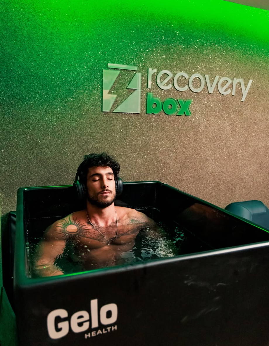 Atleta em imersão fria na banheira de gelo da Recovery Box, com o letreiro da marca na parede